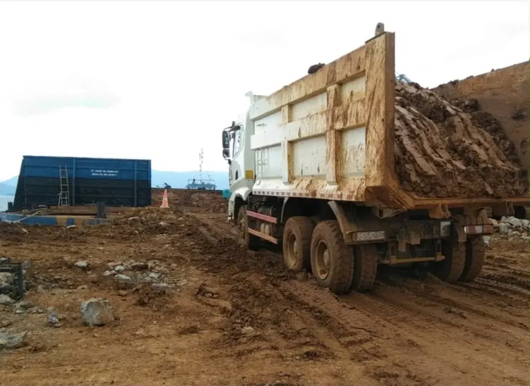Truck carrying ore beside barge-loading infrastructure in a supplied photograph